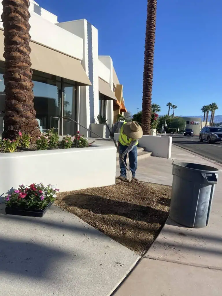 Landscaping worker preparing soil for planting flowers near commercial building.