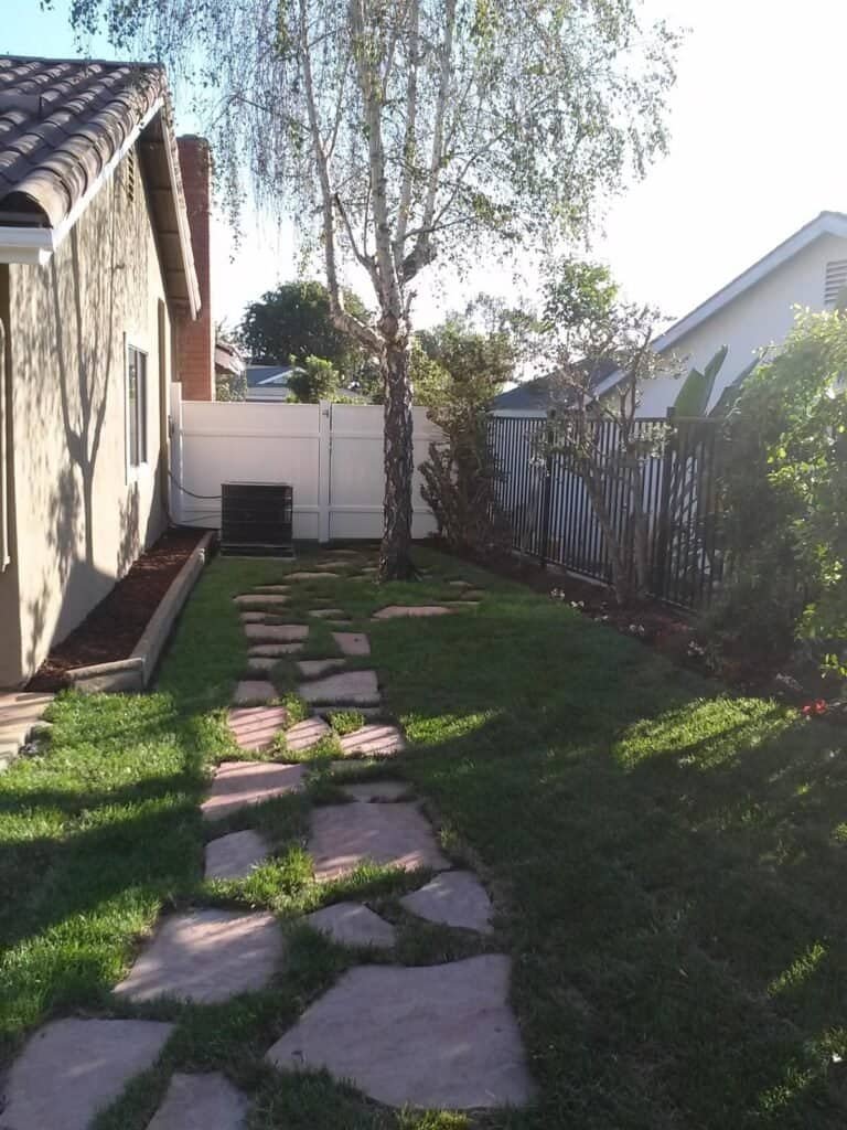 Beautiful backyard with stone pathway, lush grass, and mature trees offering privacy and aesthetic appeal.