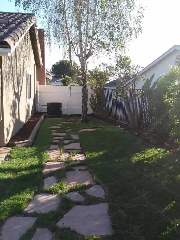 Beautiful backyard with stone pathway, lush grass, and mature trees offering privacy and aesthetic appeal.