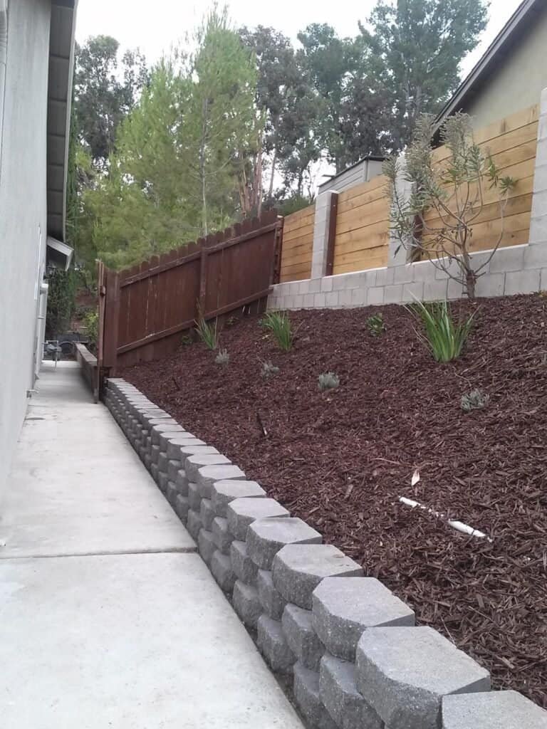 Durable concrete block landscape wall with garden soil and plants in backyard landscaping design.