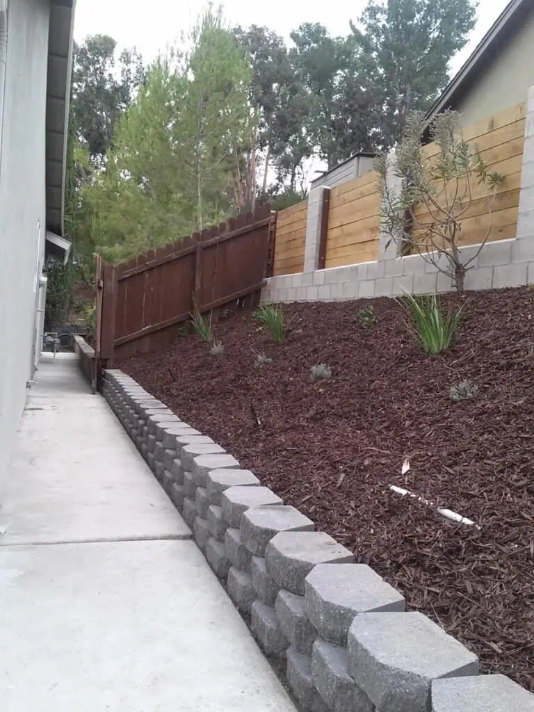Durable concrete block landscape wall with garden soil and plants in backyard landscaping design.